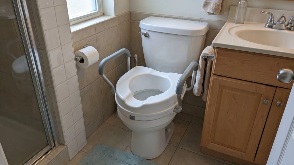 Raised toilet seat with handles in a tight bathroom space near a vanity
