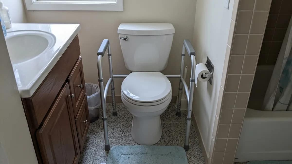 toilet safety frame installed with limited side clearance next to a vanity and wall in a small bathroom